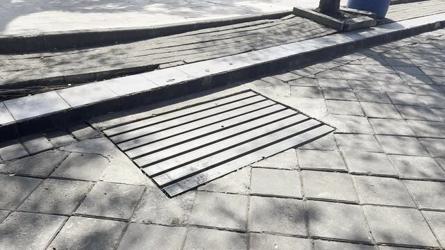 Metal drainage grate on urban sidewalk paving blocks background