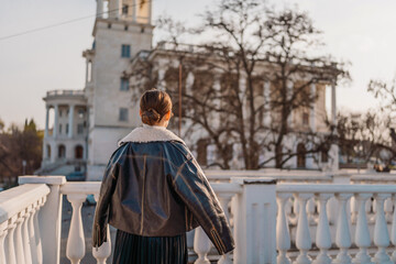 Fototapeta premium Woman leather jacket architecture standing on a white stone balcony overlooking a historic building in the city during sunset