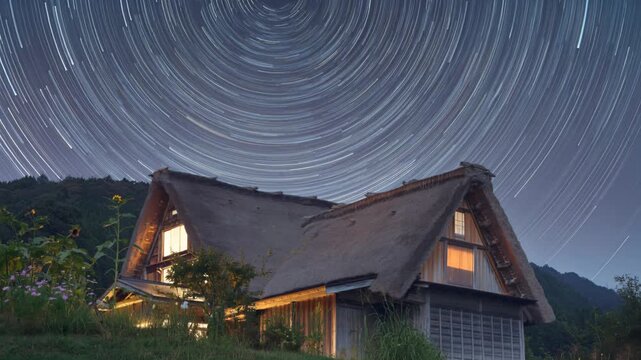 Star trails arc above thatched roof Japanese farmhouse at twilight