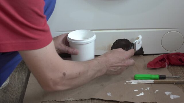 Painting a rusty metal panel of a washing machine, Man applying white putty filler to rusty damaged parts of washing machine