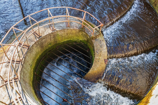 Water flows down a concrete structure into a collector. A small river or stream is directed underground. A round spiral drain with metal grates, surface runoff (stormwater, meltwater, rainwater)