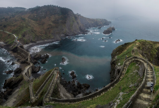 High angle panoramic view of the famous stone steps path carving through the cliffs to Gaztelugatxe hermitage on a moody overcast day in Spain