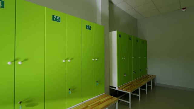Lockers line wall above long wooden benches in empty sports changing room. Clean minimalist interior offers quiet and organized environment