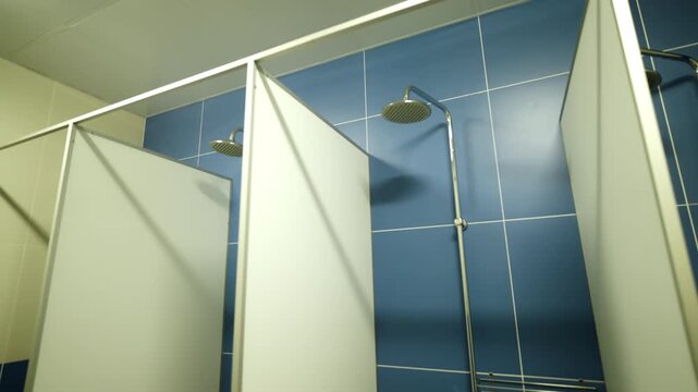 Chrome shower head stands mounted on tiled wall between partition stalls. Public bathroom facility offers refreshing space for athletes