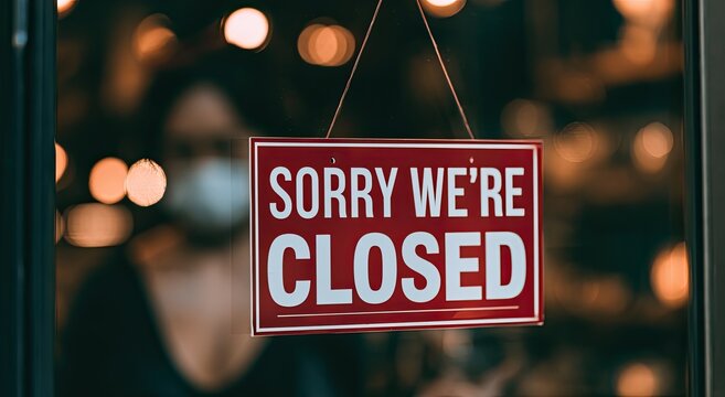 Red "SORRY WE'RE CLOSED" sign hanging in a window, blurred person behind