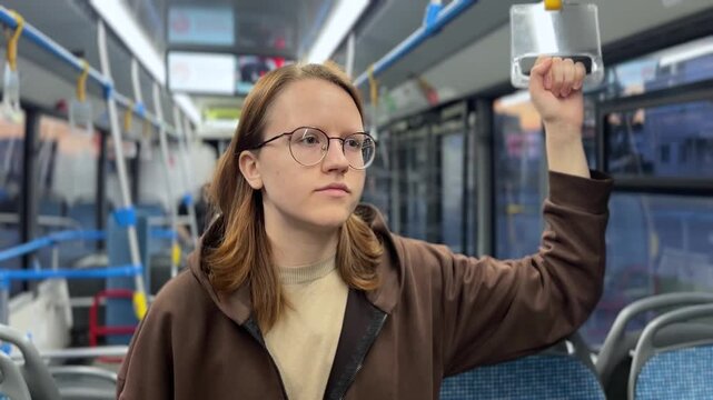 A woman stands inside a bus, holding onto a grab pole. The woman looks focused as she prepares for her stop in the spacious bus interior.
