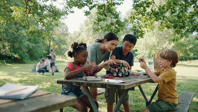Teacher Helping Kids Assemble Educational Robot Outdoors