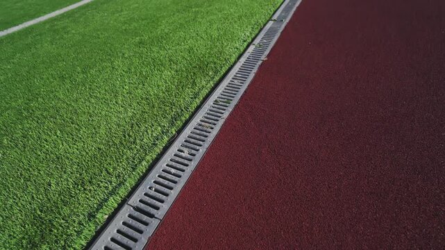 Metal drainage grate divides turf and rubber running track. Clean textured surfaces look ready for active outdoor sports training sessions