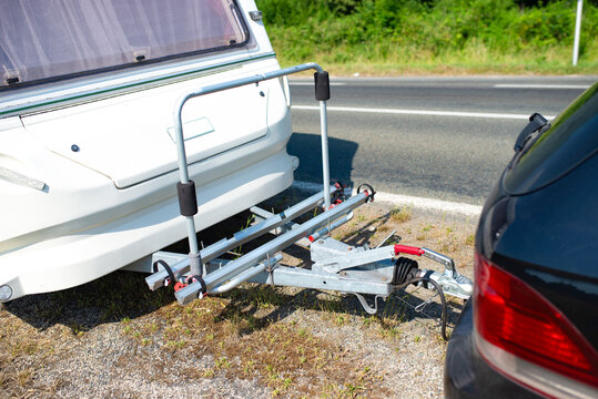Close view of a caravan towing hitch connected to a car on a sunny roadside. Travel trailer coupling, road trip transport and camping equipment.