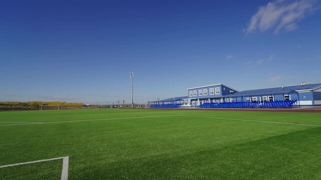 Modern sports complex building with stands sits under bright sky. Empty pitch looks ready for upcoming match during quiet twilight hours