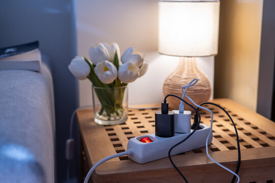 Power strip with multiple chargers plugged in, illuminating with a red switch, promoting themes of electricity consumption, energy saving, and efficient power usage in a cozy room setting