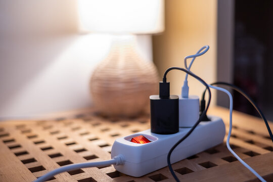 Power strip with an illuminated red switch and various device chargers plugged in, symbolizing electricity consumption, energy savings, and efficiency in modern homes
