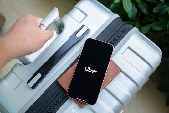 Man hands holding phone Apple iPhone 17 Pro Max in Cosmic Orange outdoors on suitcase and passport holder, displaying Uber ride sharing app taxi on the screen