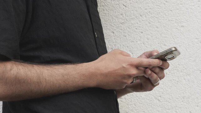 Close-up of Man Typing on Smartphone Against White Textured Wall