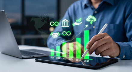 Fototapeta premium Sustainable business financial investment concept with a businessman analyzing a rising green growth chart and carbon reduction icons on a digital tablet.
