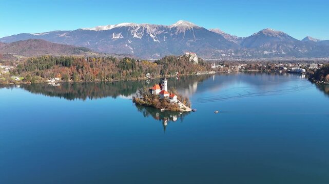 Aerial drone view of the iconic Church of the Assumption on Lake Bled island surrounded by crystal-clear water and the Julian Alps in autumn. Scenic panoramic landscape of Bled, Slovenia, one of 