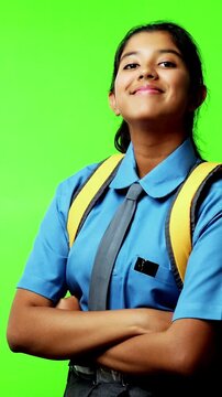 Portrait of Indian Asian teenage girl in school uniform with backpack, smiling confidently against green chroma screen, looking at camera with happiness, enthusiasm, symbolizing education, success