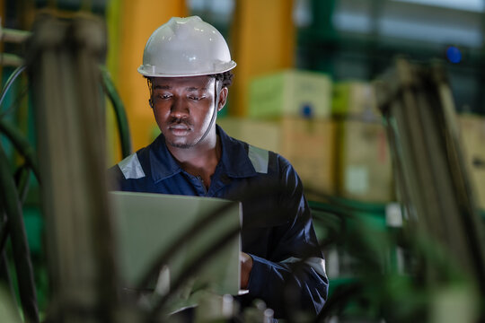 Industrial technician using laptop to review machine performance and maintenance records on factory floor. Smart manufacturing, digital inspection, predictive maintenance, Industry 4.0 operations.