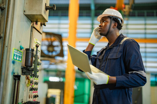 Engineer evaluates equipment status with laptop before modifying machine controls inside production facility. Industrial engineering, preventive maintenance, process optimization.