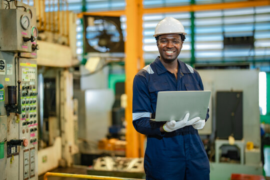 Industrial worker smiles while holding laptop inside manufacturing facility after completing production inspection. Engineering success, factory operation, workplace achievement, manufacturing process