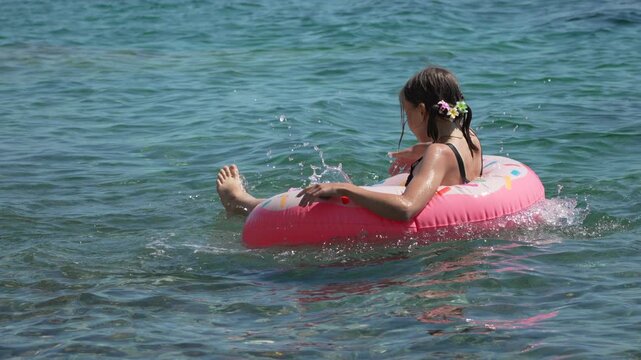 Girl floating swimming, joyful young girl playing with a donut inflatable ring in the sea during a sunny summer vacation on the beach