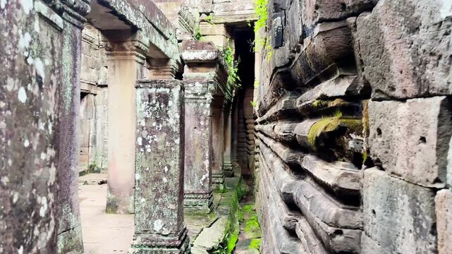 Cinematic footage of a narrow stone corridor inside the ancient Bayon Temple in Angkor Thom, Cambodia. Featuring weathered sandstone walls, carved architectural details, moss-covered stones, and
