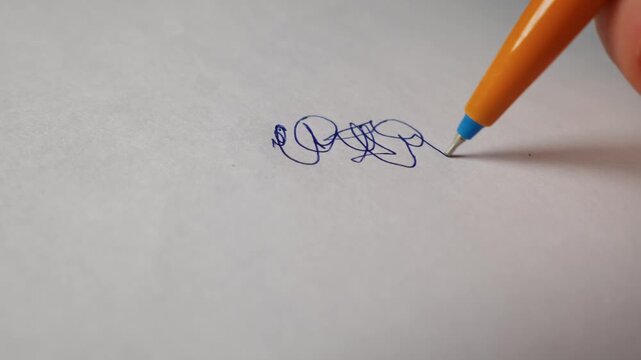 A hand holds an orange ballpoint pen to sketch a blue ink doodle on clean white paper. The macro shot captures the fine tip of the pen creating a looping shape under bright light.