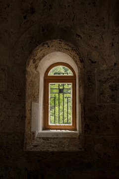 An ancient arched wooden window, set deep into the thick, textured stone wall of Haghartsin Monastery in Armenia, lets light into the room.