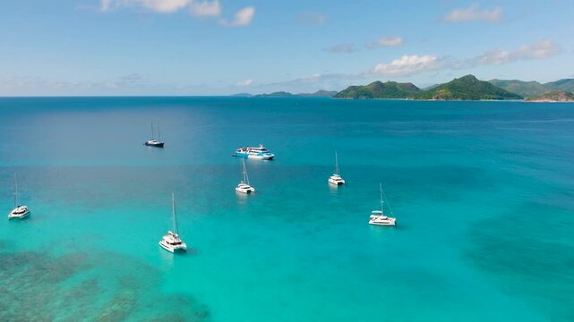 Anchored yachts in a turquoise bay with a view of distant islands under a clear sky. Seychelles, La Digue.