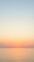 Obraz premium Serene ocean horizon at sunset with soft peachy and coral tones fading into pale blue sky, calm water surface reflecting warm light, tranquil seascape for relaxation and wellness projects.