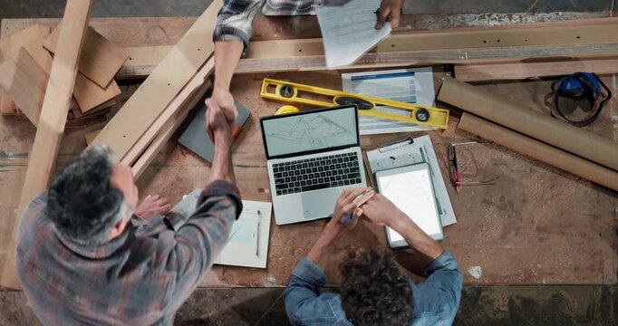 Carpenter, team and handshake in workshop with paperwork, design update and agreement. Above, men and shaking hands at laptop for woodworking project, feedback and task delegation for productivity