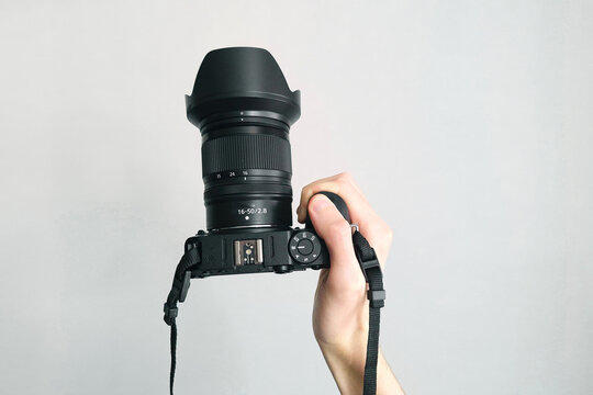 Human hand firmly holds professional camera with lens hood pointing forward on white background