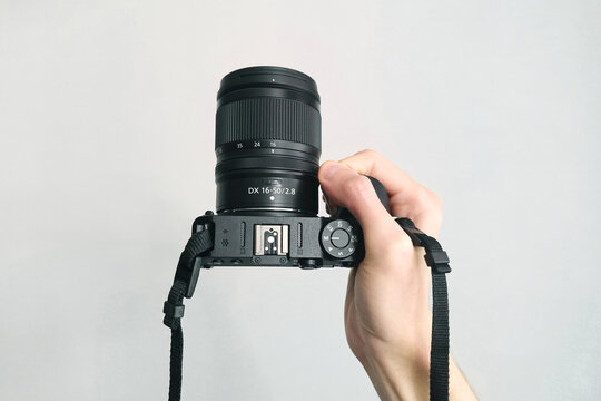 Professional photographer hand holds modern black camera with lens against clean background.