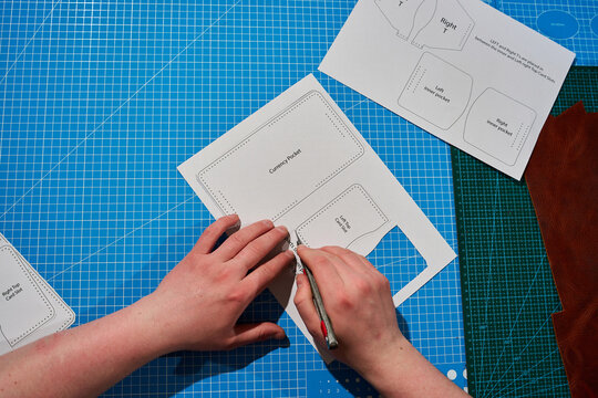 Artisan using a precision knife to cut a printed paper pattern on a blue cutting mat.