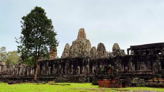 Wide cinematic view of the ancient Bayon Temple in Angkor Thom, Cambodia, featuring its iconic stone towers surrounded by lush greenery. This historic Khmer masterpiece, located within the UNESCO
