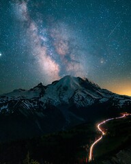  Majestic astrophotography landscape of the Milky Way galaxy over a snow capped mountain peak with car light trails on a winding valley road © Baby khan