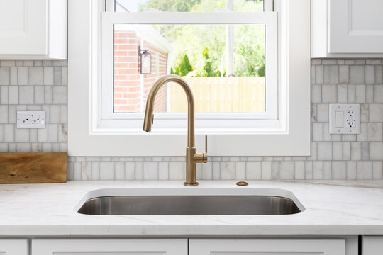 A kitchen detail with white cabinets, gold faucet, marble tiled backsplash, and a granite countertop.