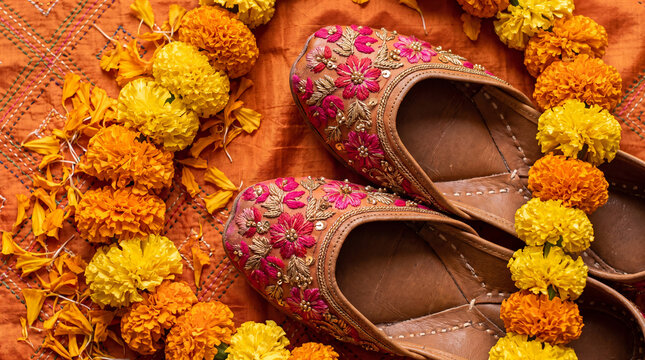 Pair of brown embroidered jutti shoes with marigold garland on orange cotton fabric