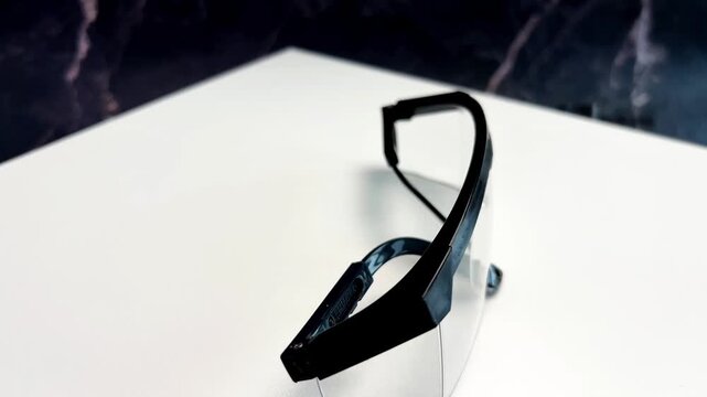 Close-up of protective transparent construction goggles with black piping slowly spinning on a white podium in the center. Repair concept, protective equipment, eye protection. High quality 4k footage