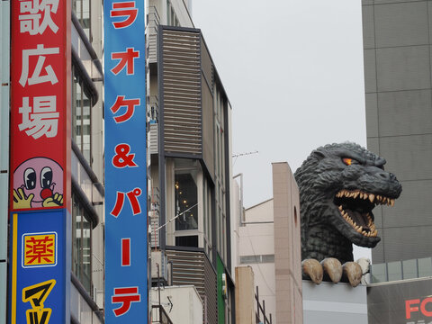 TOKYO, JAPAN - January 7, 2025: Shinjuku with signs on a a Matsumoto Kiyoshi drugstore and Karaoke Kan karaoke center and a statue of Godzilla on a Toho movie theatre.