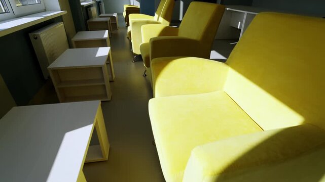 Row of armchairs stands opposite neat tables under natural light. Quiet vacant workspace offers comfortable area for office employees