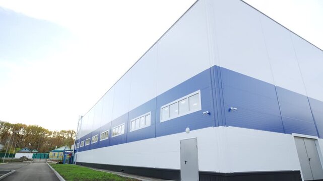 Warehouse facade features geometric design and fresh asphalt roads. Neat lawn borders surround newly constructed commercial building