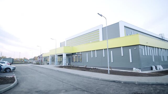Sports complex building features grey and yellow facade panels. Freshly asphalted roads surround exterior area during construction work