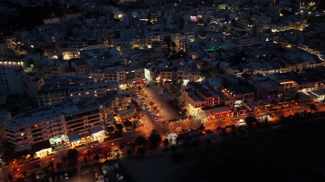 Aerial drone view of the illuminated town streets and seafront promenade glowing at night, Rethymno, Greece