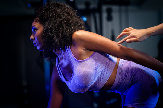 Strong woman fitness: an athletic Black woman training her back with a bent-over dumbbell row inside a moody fitness studio, mid repetition, captured in a cinematic fitness portrait
