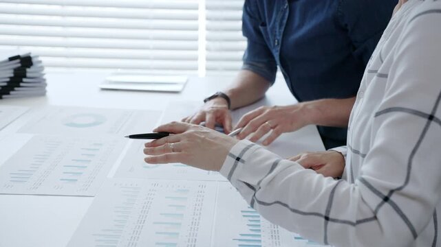 Business professionals analyzing financial data and working together, reviewing charts, graphs, and documents on a white desk during an important office meeting to strategize future growth