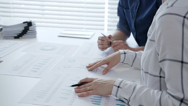 Business professionals analyzing financial data and working together, reviewing charts, graphs, and documents on a white desk during an important office meeting to strategize future growth