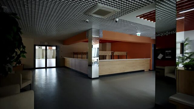 Lobby of modern sports complex shows massive wooden reception counter. Sunlight from distant glass entrance floods expansive clear space
