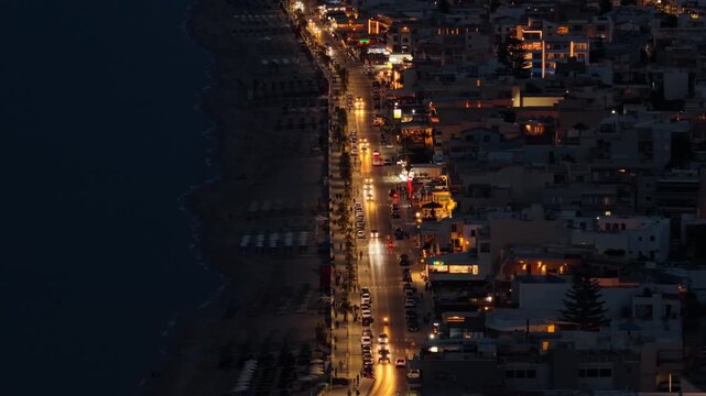 Aerial drone view of the illuminated beachfront avenue at night beside the sandy town beach, Rethymno, Greece