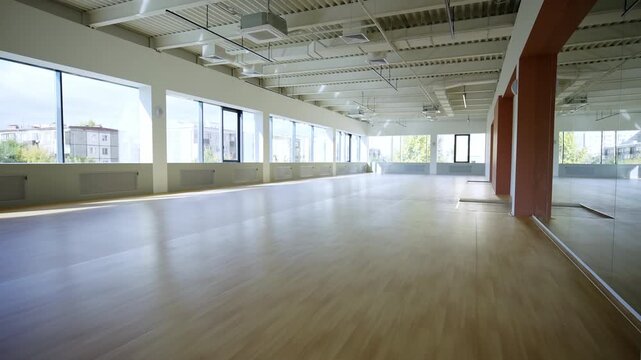 Spacious hall with clean walls stands ready for athletes and dancers. Polished wood floor gleams under daylight streaming from windows